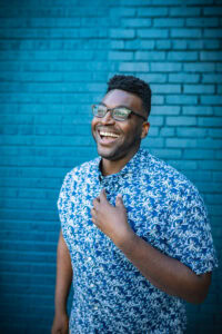 Jamar Diggs, a YouTube consultant, standing against a blue wall, laughing.